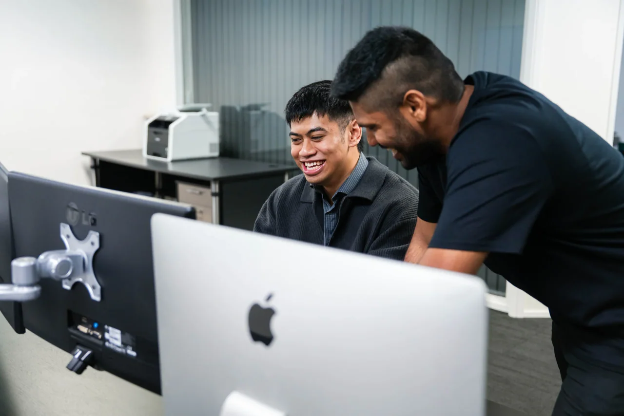 Two Mint team members smiling as they work through a problem on a computer