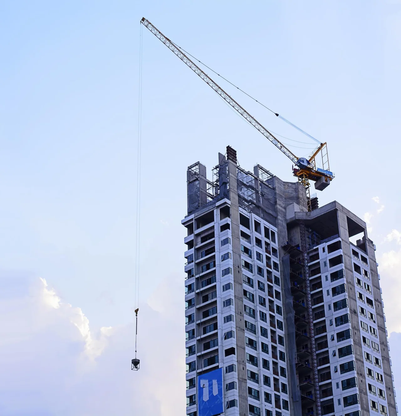 A tower crane lifting a concrete bucket beside a high-rise under construction