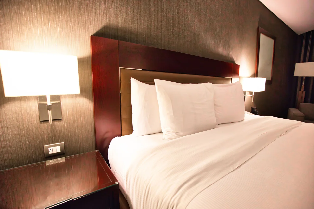 A hotel room with a made bed and lit bedside lamps