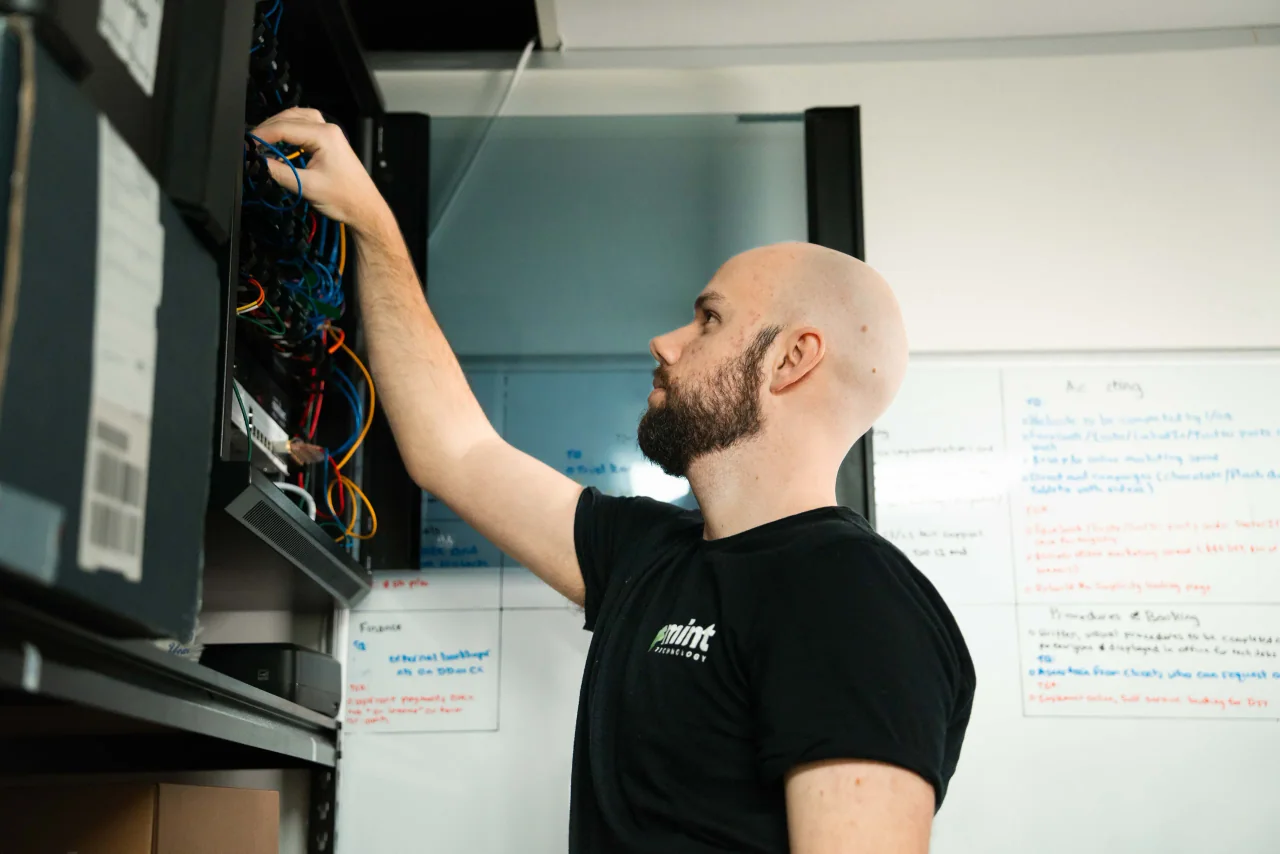 A Mint technician patching network cables in a comms cabinet