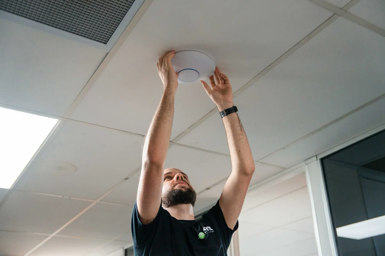 A Mint technician fitting a WiFi access point to an office ceiling
